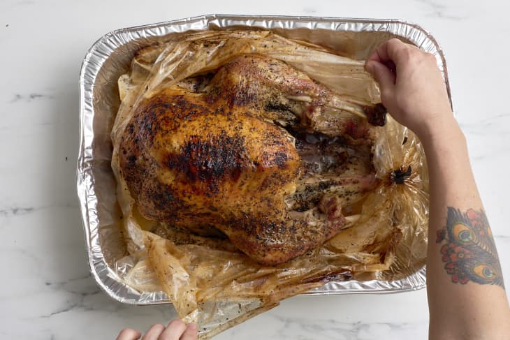 Hands opening a bag containing a roast turkey.