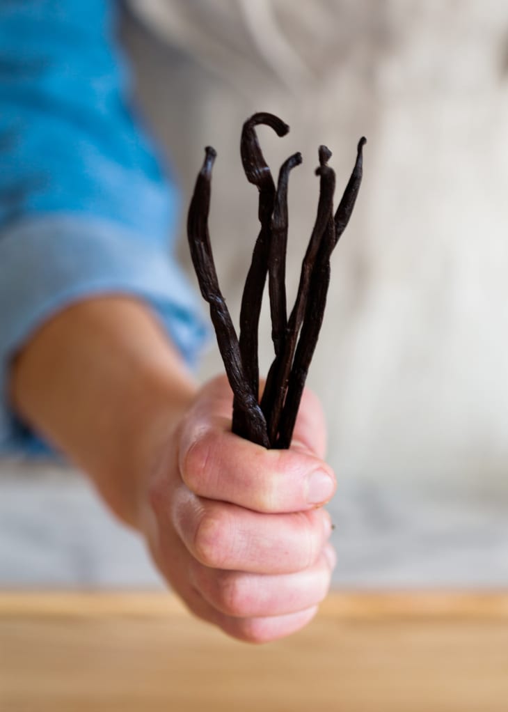 A person holds five vanilla beans in one hand