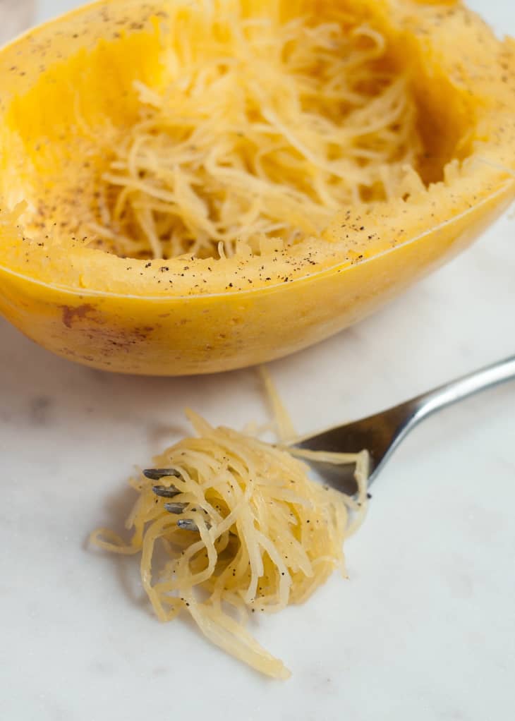 Spaghetti squash has been scraped and a fork beside it with spaghetti squash strands around it