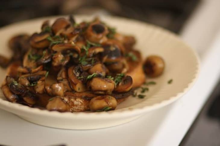Cooked mushrooms garnished with thyme are served on a white plate