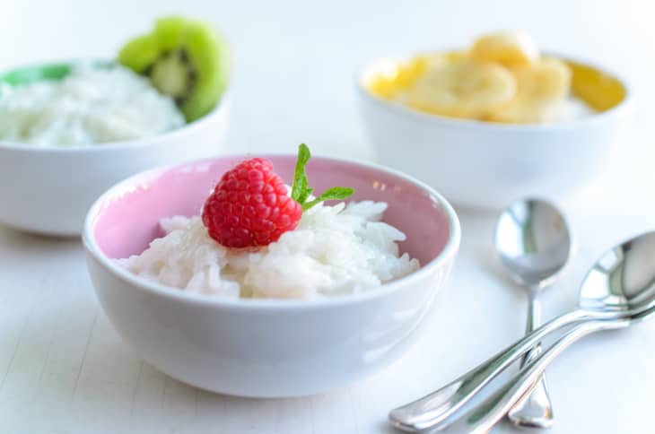 Thai sticky rice pudding with coconut milk, topped with raspberry, in a bowl, with spoons on the side