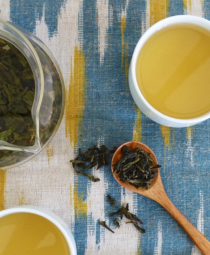 Dried oolong leaves on a wooden spatula, with oolong tea on the side