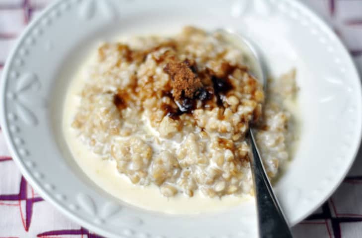 A silver spoon is placed in a white bowl of steel-cut oats soaked in milk and topped with brown sugar and syrup.