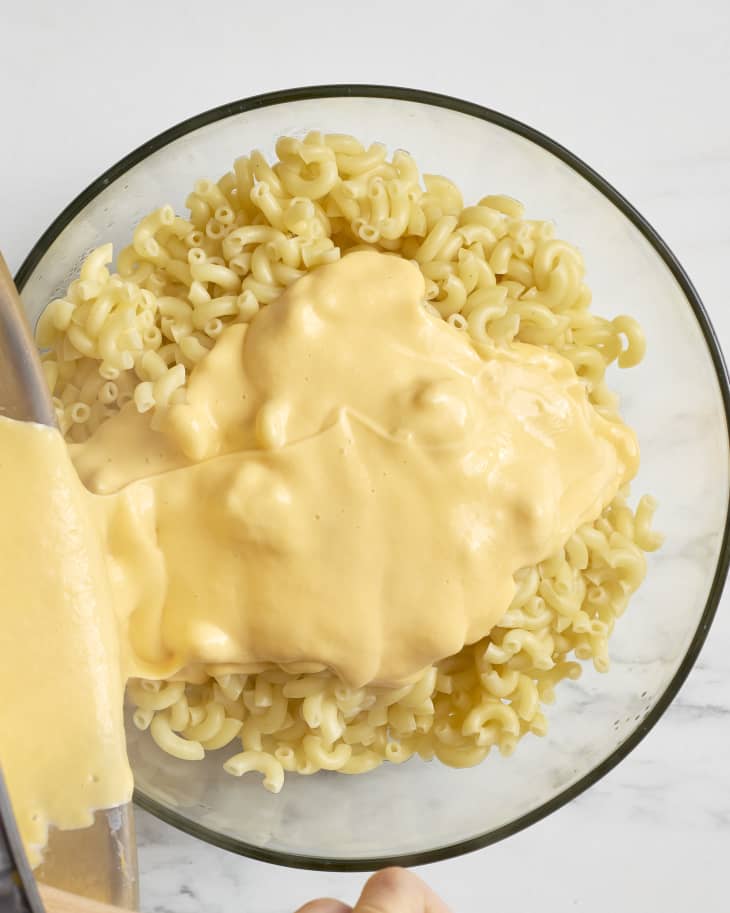 Pouring cheese sauce over a bowl of cooked macaroni pasta
