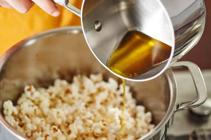 Pouring melted clarified butter or ghee into pot of popped popcorn.