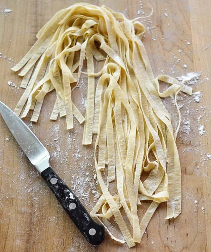Fresh, uncooked pasta noodles laid out on a cutting board with a knife