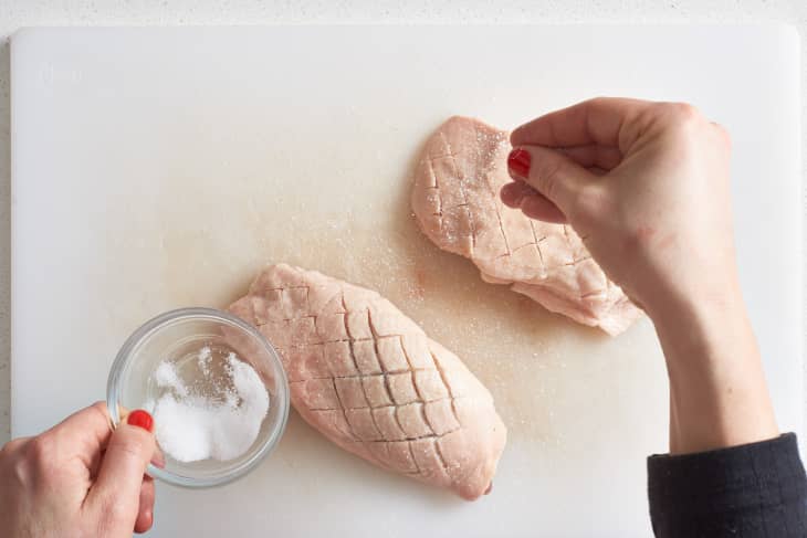 A woman sprinkles salt on top of duck breasts' cut into crisscross