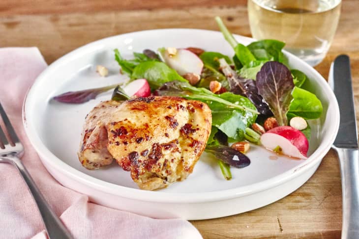 Plate with oven-roasted chicken thigh alongside salad with nuts and apple slices