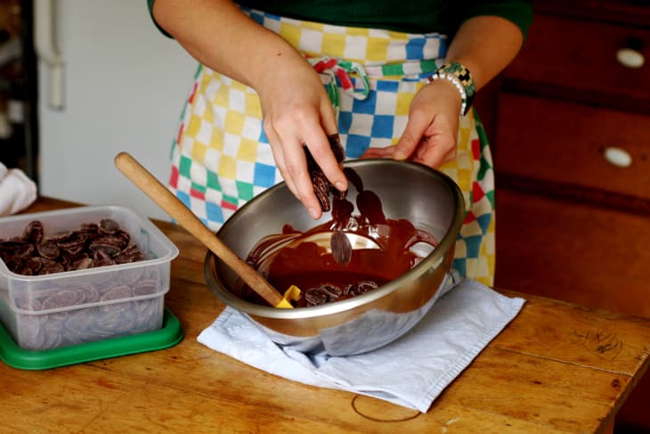 Chocolatier Alexandra Whisnant puts chocolate pieces into a mixing bowl with a spatula in it