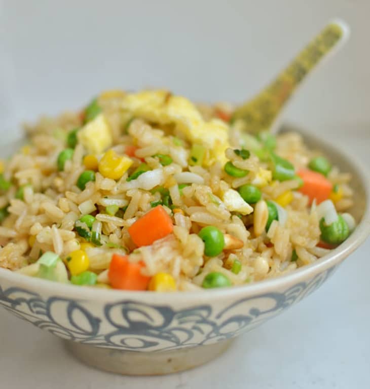 Bowl of fried rice with small pieces of scrambled egg, carrots, peas, corn, and scallions
