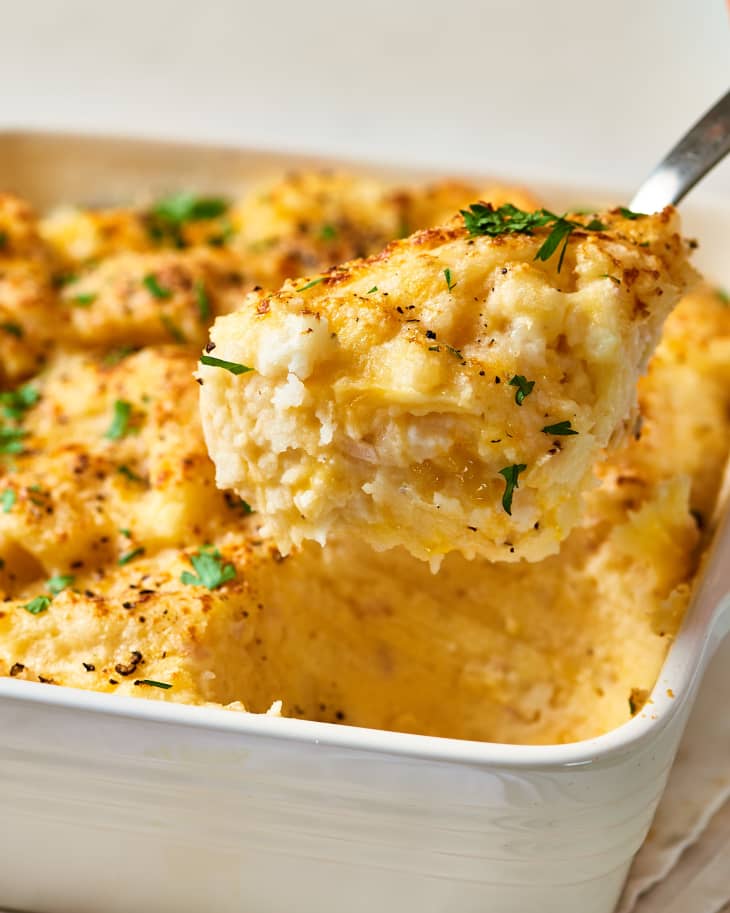 A spoon is lifted up with a serving of smashed potato casserole