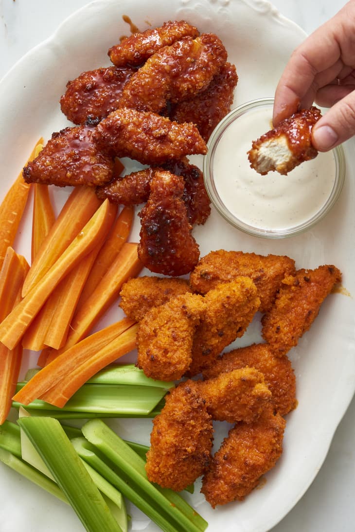 Someone dips the baked boneless chicken wings in a dressing, with slices of carrots and celery served on the side