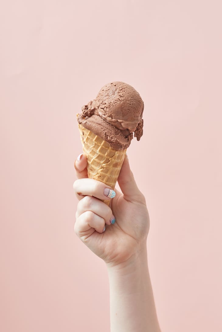 A person holds a chocolate ice cream in a cone