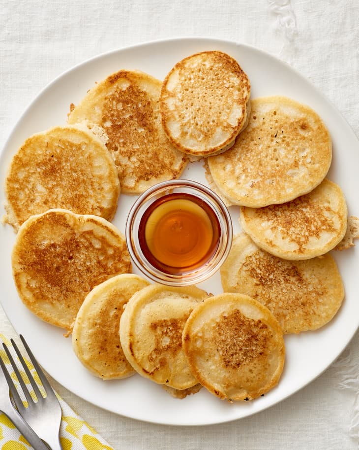 Pancakes laid out in a circle on a plate with a small dish of maple syrup in the center