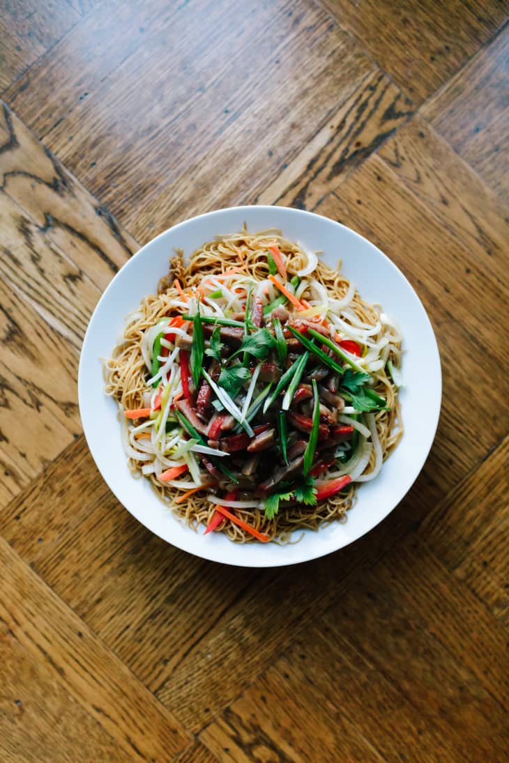 Stir-fried noodles topped with colorful vegetables, green onions, and cilantro in a white bowl.
