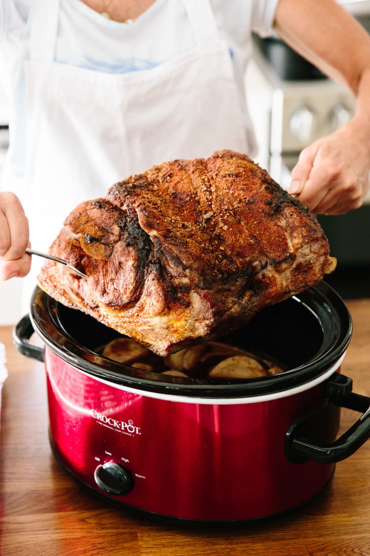 A slab of pulled pork inserted in a fork is lifted up from a red-colored CrockPot