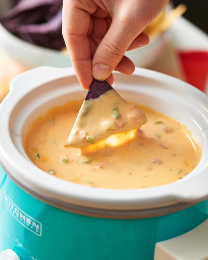 Someone dips a nacho in a bowl filled with cheese sauce