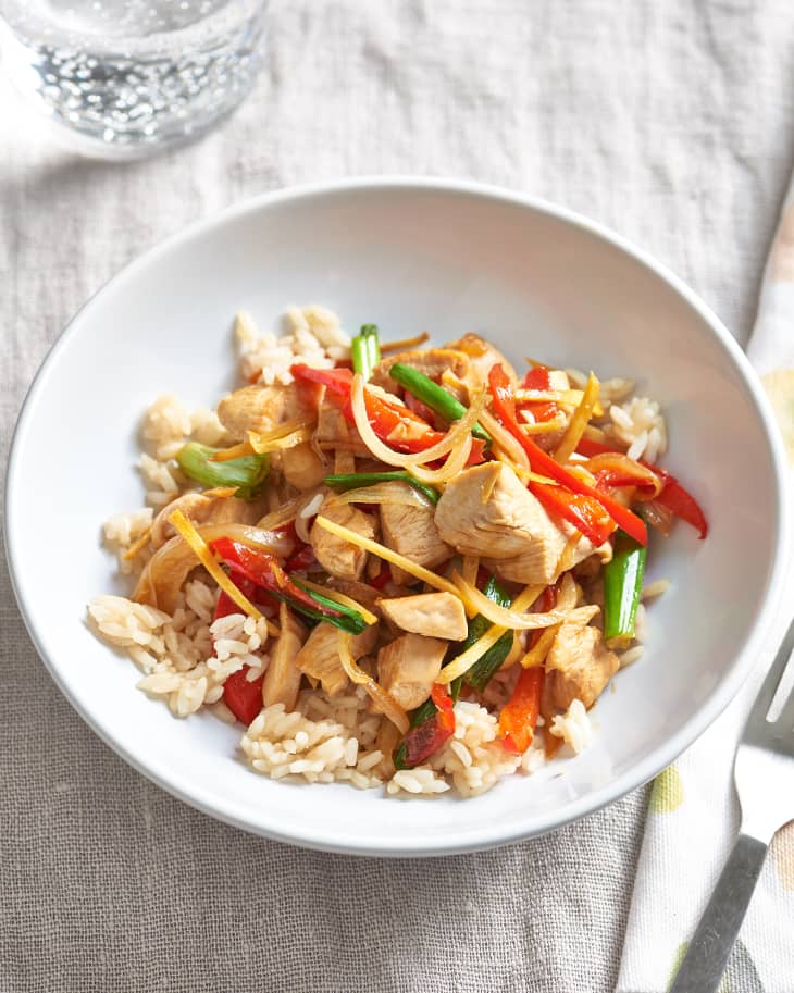Thai ginger chicken stir-fry, cooked with onions, bell peppers, scallions, over white rice in bowl