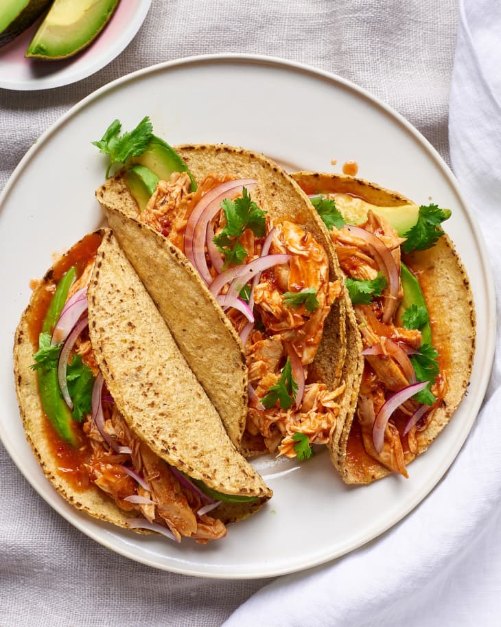Three tacos filled with slow-cooker chicken tinga filling with garnishes of pickled onion, avocado, and cilantro