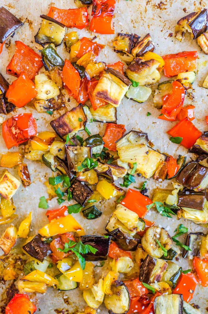 Roasted chopped vegetables on a sheet pan, including red and yellow bell peppers, eggplant, and zucchini