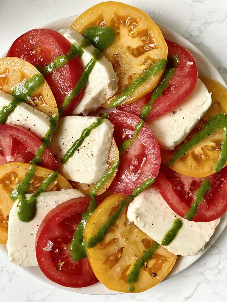 plate of tomatoes, orange and red tomato slices, large slices of mozzorella, drizzle of green sauce