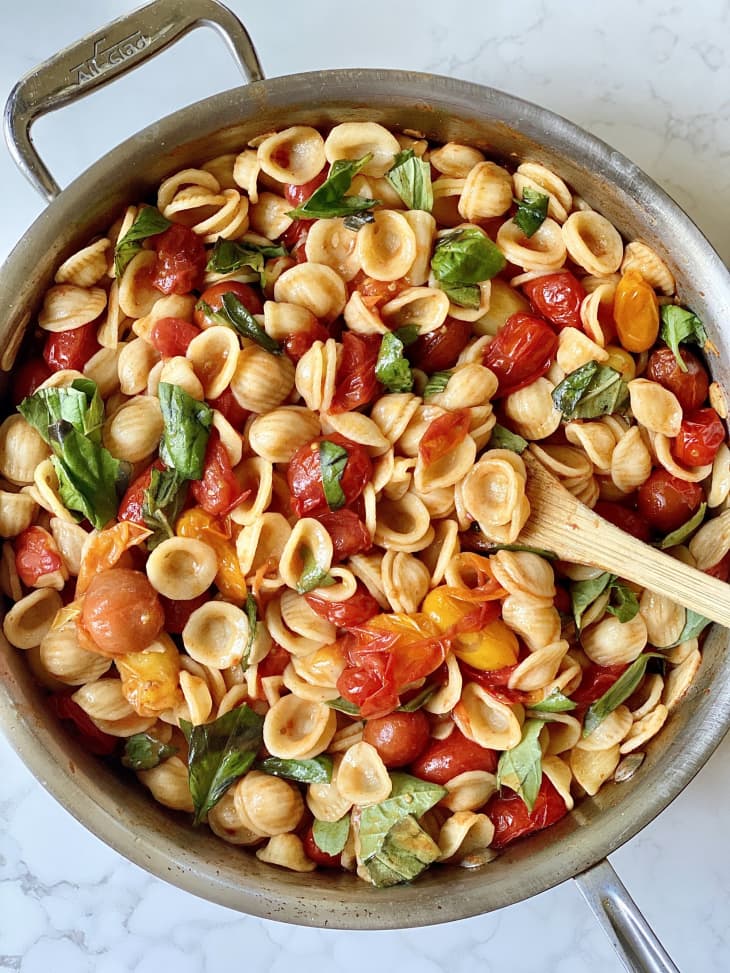 pot of pasta, mini shell noodles, basil, cherry tomatoes, wooden spoon, stove top