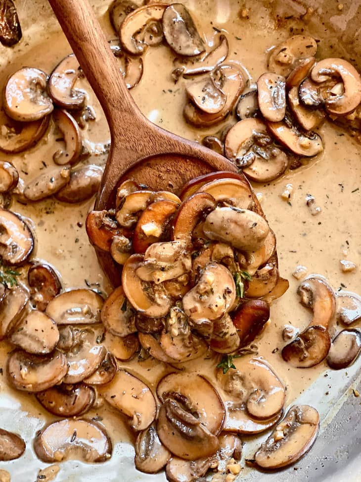 mushrooms in cream sauce in skillet with wooden spoon