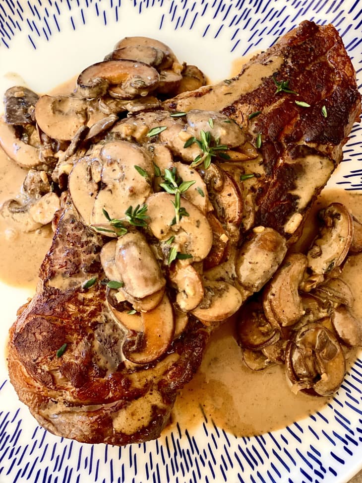mushrooms in cream sauce on top of steak with thyme garnish