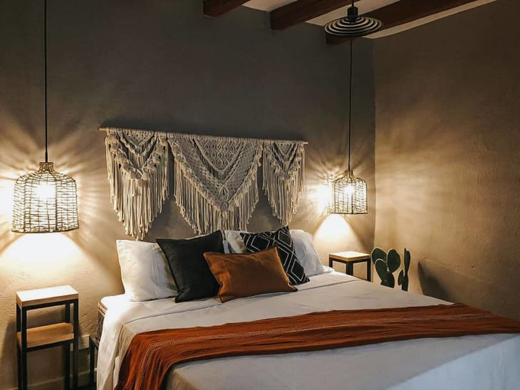 a bedroom features black, white and burnt orange accents with an oversized macrame wall hanging above the bed