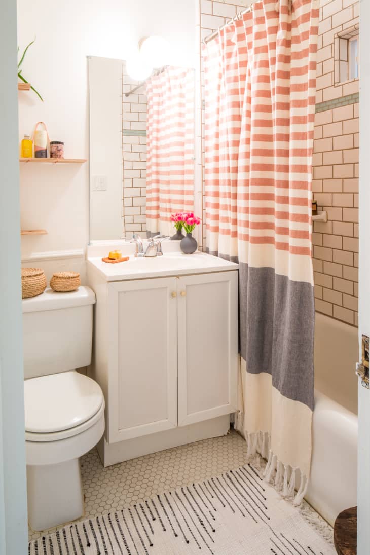 A small bathroom with a shower curtain dividing the vanity from the shower.