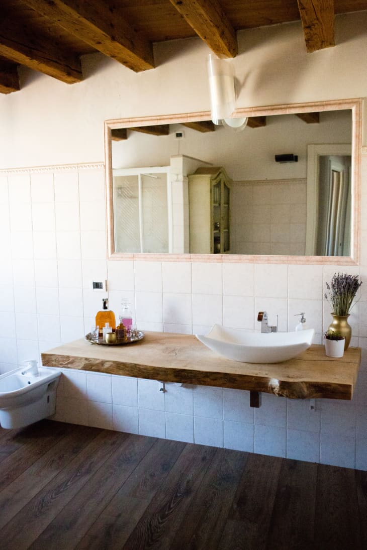 A bathroom with a large natural wooden counter and rough timber ceiling.