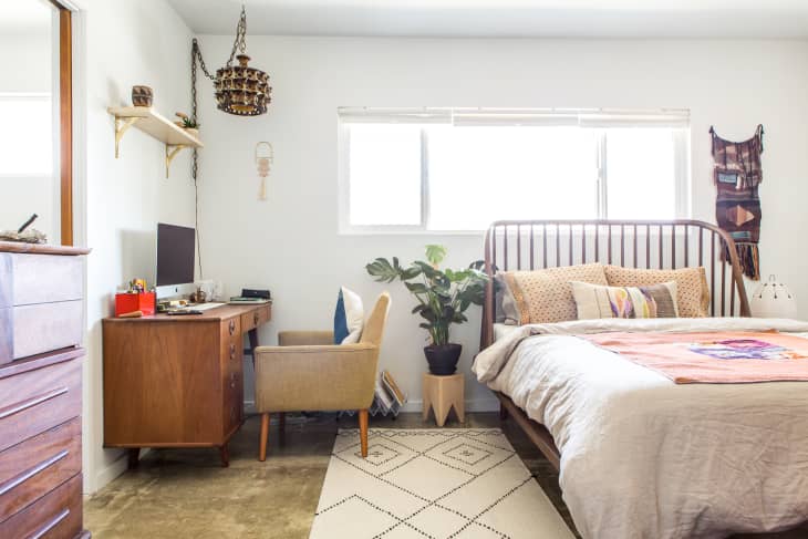 a large Monstera plant sits between a desk with chair and the bed in this bedroom