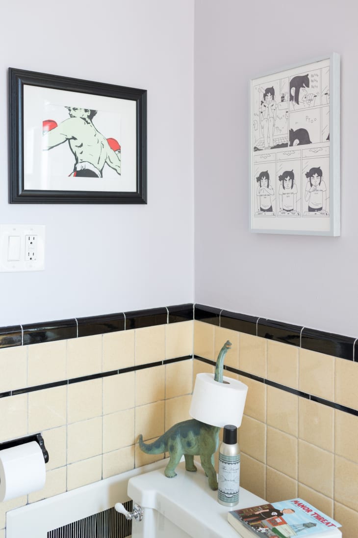 A bathroom with comic book artwork and a dinosaur toy used as a toilet paper holder.