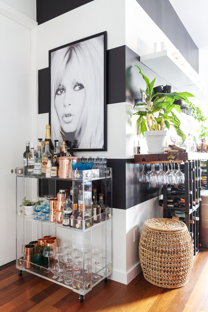 A corner of a home decorated with a bar cart with barware and a wall painted with black and white stripes with a black and white framed photo