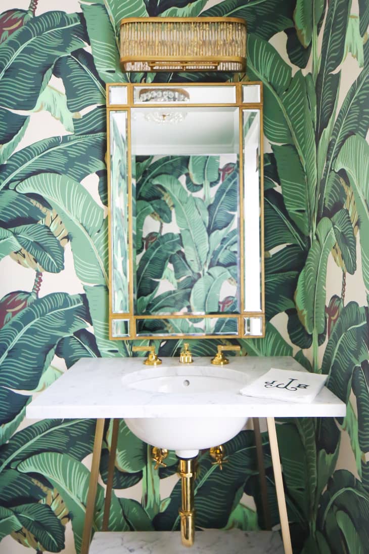 A bathroom with tropical-leaf-patterned wallpaper.