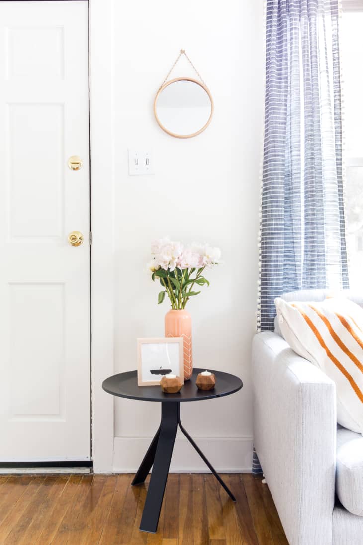 A simple white foyer with a small round black table at the entry holding a vase of white flowers
