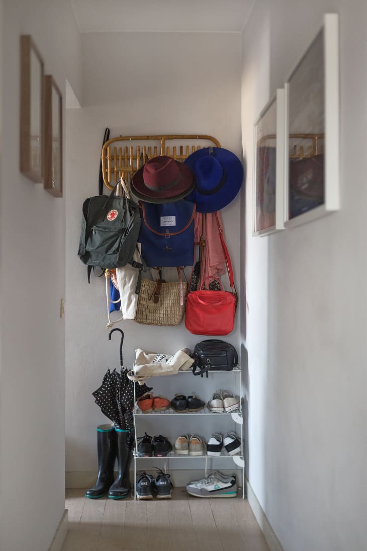 A narrow entryway with a wall-mounted rack above a shoe rack full of shoes, backpacks, hats, and other accessories