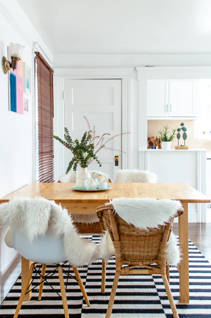 A dining room table on checkerboard flooring with sheepskin rugs on the chairs.