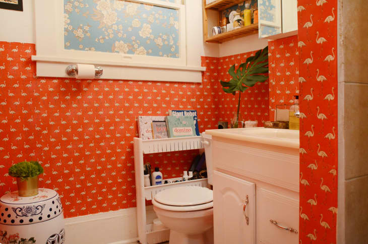 A quirky bathroom with orange wallpaper with pink flamingos on it.