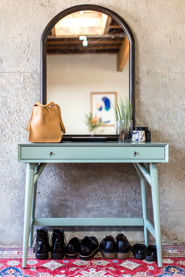 A light blue entryway table with an arched mirror leaning on top