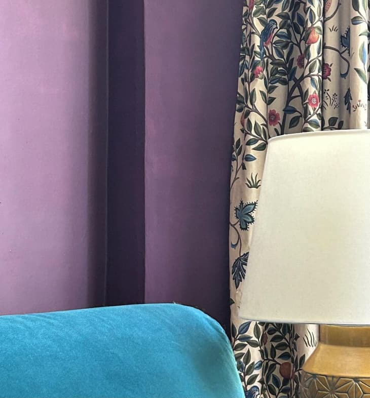 a corner sitting area features bright purple paint and a teal velvet chair with curtains featuring both hues