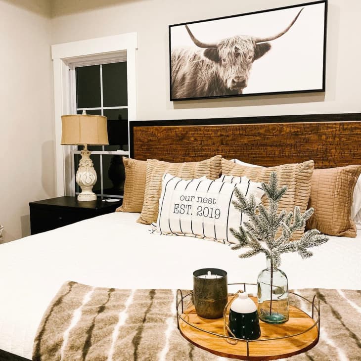 a rustic bedroom with throw pillows and an oversized cow print on the wall above the wooden headboard