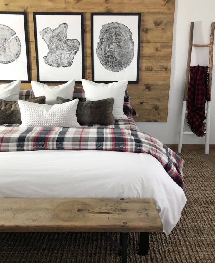 a rustic bedroom includes wooden accents, plaid bedding and wood-cuts as printed art above the bed