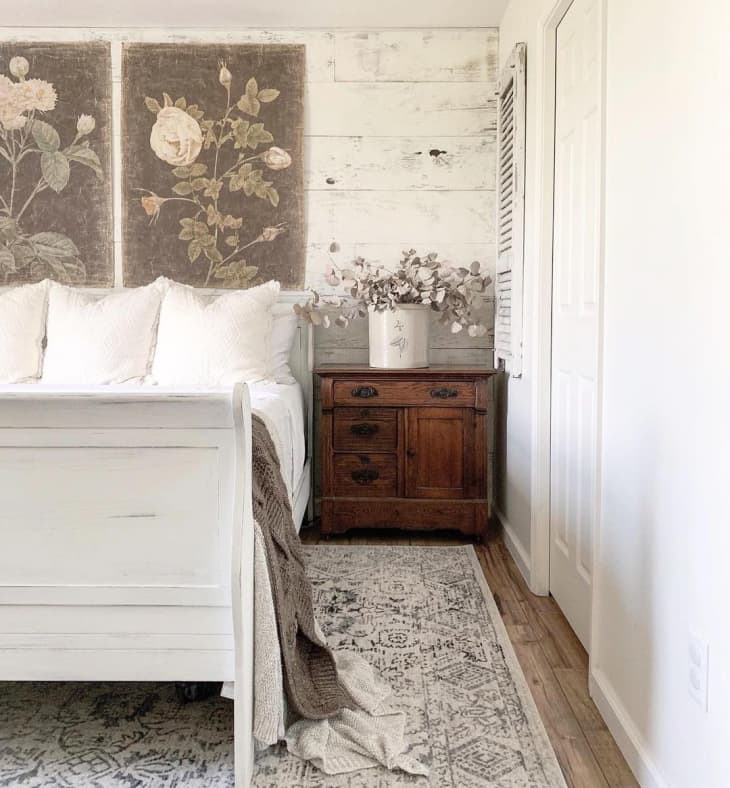 a rustic bedroom with white-washed wooden accent wall and muted floral wall hangings above the bed
