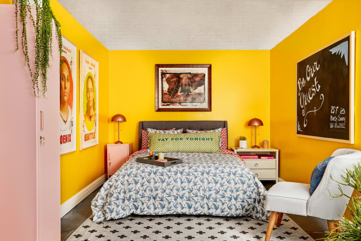 Guest room with colorful patterned bed linens, bright yellow walls, large sports posters, chalkboard saying "be our guest"