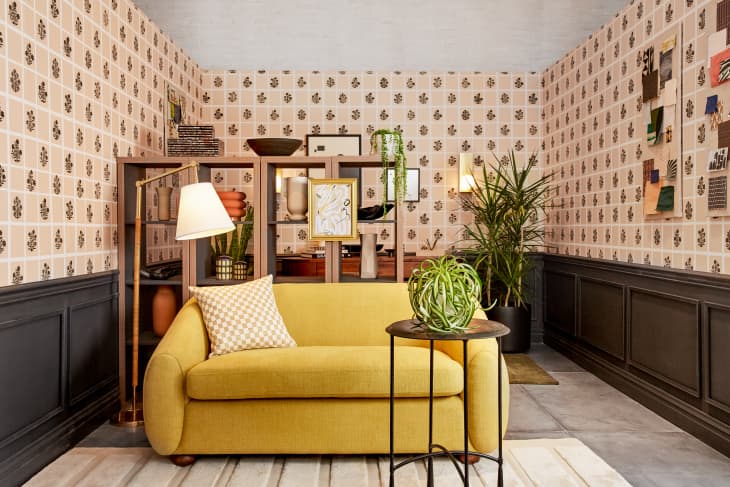 room with DIY wallpaper, gold loveseat, wood desk, shelves with l'objets, plants, gold rug
