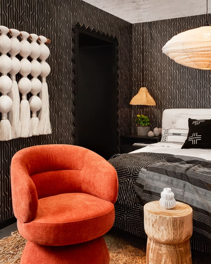 bedoom with black and gold wallpaper, white wall textiles, woven pendant lamp, orange plush lounge chairs
