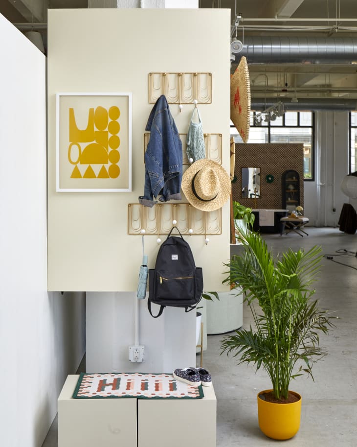 Head on view of three different sized gold coat racks hanging on a beige wall and a piece of yellow abstract art in a white frame.