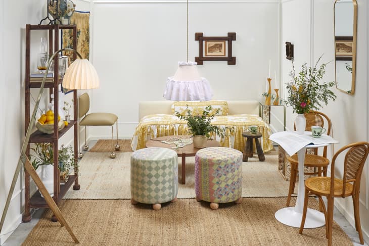 Head on view of a living room with white walls, a low couch with printed yellow and white ruffled cushions, two patchwork stools, and a small bistro table and chairs in the front right.