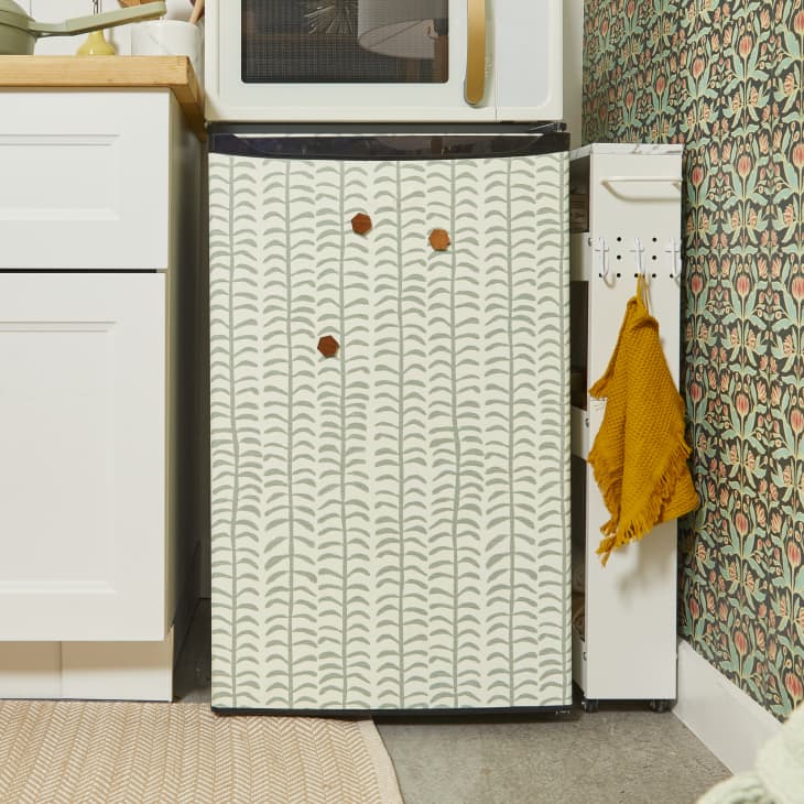 Close up view of a white and sage green patterned mini fridge, and white microwave with a gold handle on top of it.